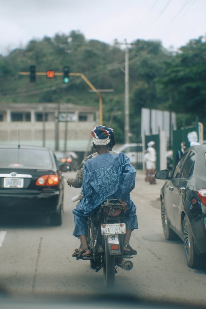 service-06 Motorcyclist wearing traditional attire navigating through busy traffic in Nigeria.