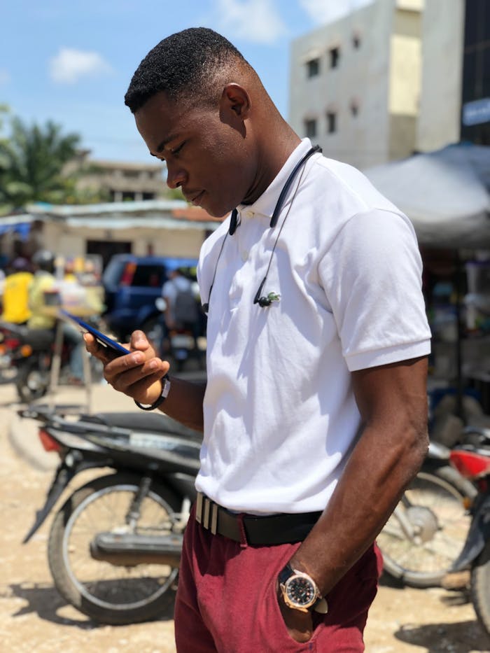 service-04 African man engaged with smartphone in a lively outdoor market setting in Ikeja, Nigeria.