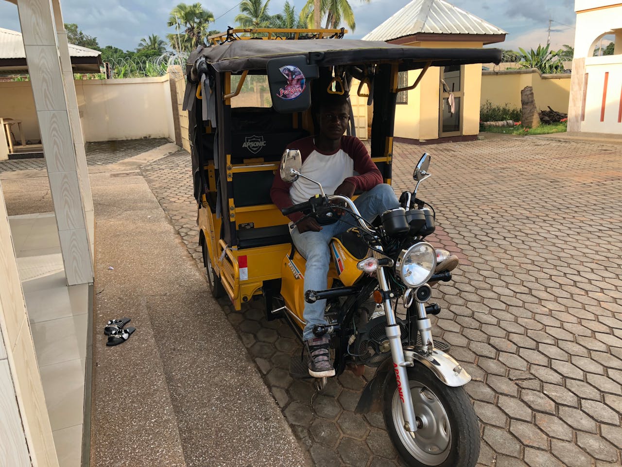our-stories A man rides a yellow tricycle outdoors in Kpando, Ghana, showcasing local transportation.
