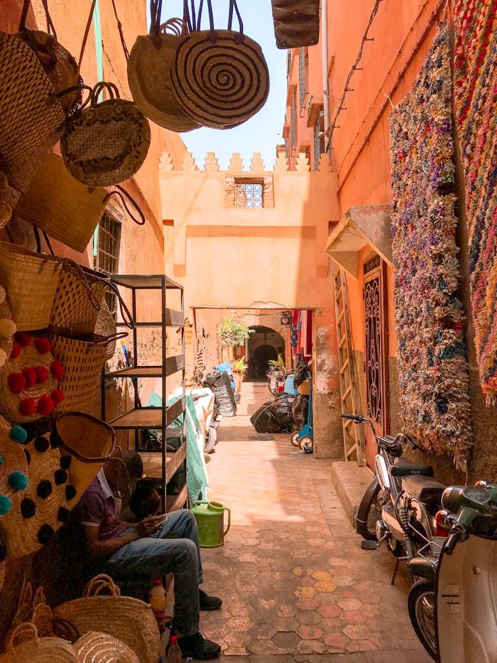 service-03 Colorful alley in Moroccan bazaar with shops, woven baskets, and motorbikes under daylight.